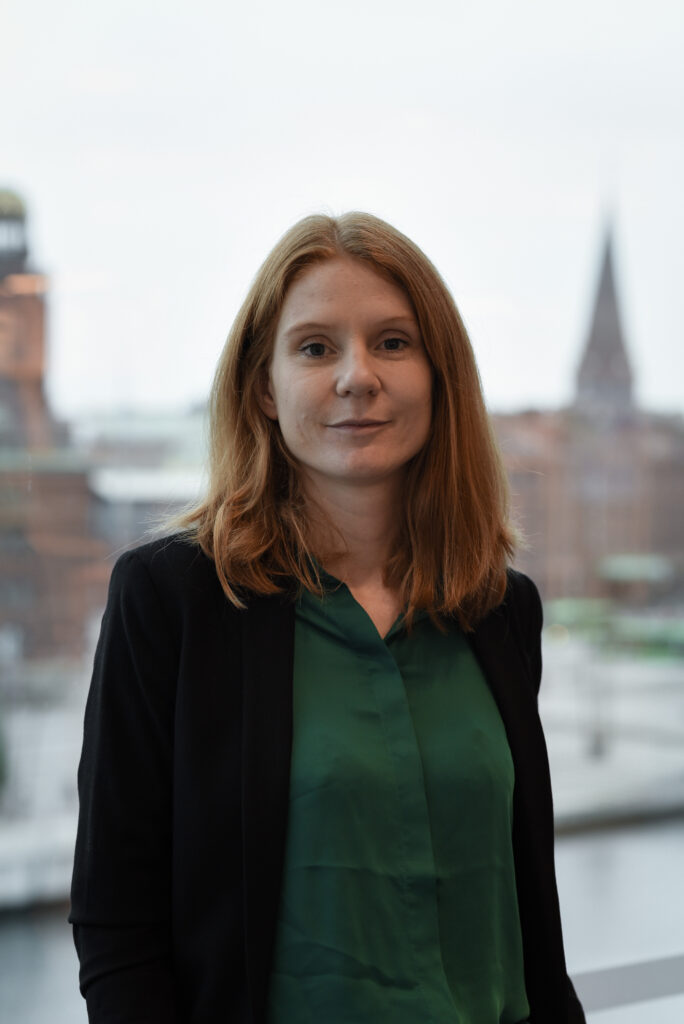 Karin Henrikz, bakgrunden är en utsuddad byggnad med torn, fotografi av Mattias Pettersson.